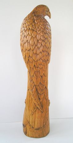 a carved wooden bird sitting on top of a tree stump in front of a white wall