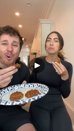 a man and woman sitting on a couch eating food from a white plate with blue designs