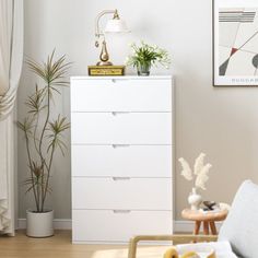 a living room with white furniture and plants on top of the dresser next to it