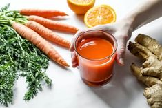 a person holding a glass of juice next to carrots and ginger