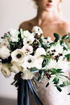 a bride holding a bouquet of white and black flowers with greenery in her hands