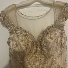 a dress hanging on a hanger in front of a white wall with beads and sequins