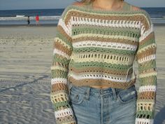 a woman standing on the beach with her hands in her pockets and looking at the camera