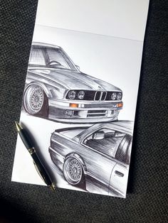 a drawing of two cars on paper next to a pen