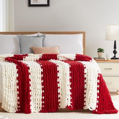 a red and white crocheted blanket is on a bed with two nightstands