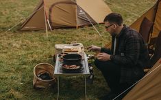 a man sitting in front of a camp stove cooking food