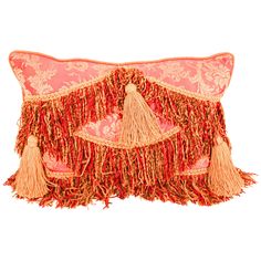 an orange and pink decorative pillow with tassels on the front, sitting on a white surface