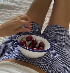 a person laying on a bed with a bowl of cherries in their lap,