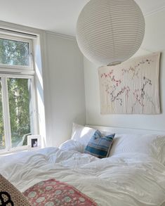 a white bed sitting under a large window next to a wall mounted art hanging above it