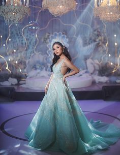 a woman in a blue dress standing on a stage with chandeliers behind her