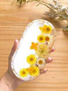 a person holding a tray with flowers in it on top of a wooden table next to plants