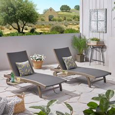 two lounge chairs sitting on top of a patio next to a potted plant and table