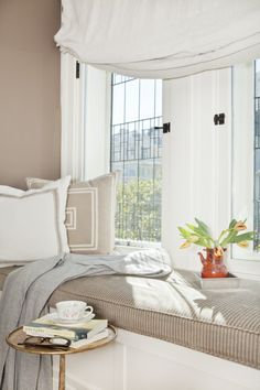 a window seat with pillows and blankets on top of it next to a potted plant