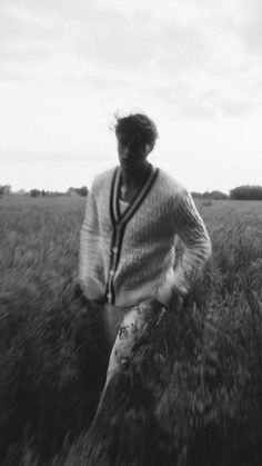 black and white photograph of a man walking through tall grass in the middle of an open field