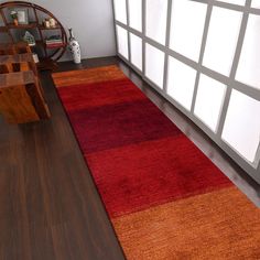 a red and orange rug on the floor in front of a wall with large windows