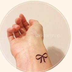 a hand with a small bow tattoo on it's left wrist, in front of a white circle