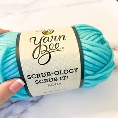 a ball of yarn is being held up by a woman's hand on a marble surface