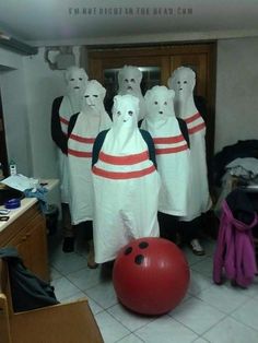 several people in white costumes with red and black bowling balls, one person is wearing an orange ball