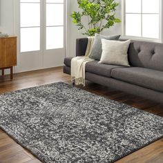 a living room with a couch, chair and rug on the wooden floor next to a potted plant