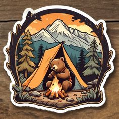 a sticker depicting a bear sitting in front of a campfire with mountains and trees