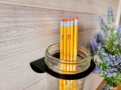 three pencils are in a jar on a shelf next to some flowers and a vase