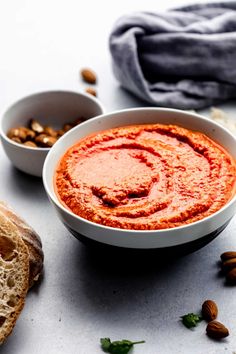 a white bowl filled with red sauce next to two bowls of bread and almonds