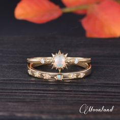 two gold rings with opal and diamond accents on a wooden table next to a flower