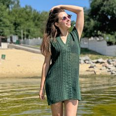 a woman standing in the water with her arms behind her head, wearing sunglasses and a green knitted dress