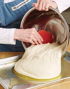 a person in an apron is kneading dough into a bowl on a metal pan