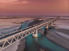 an aerial view of a bridge spanning the width of a frozen river at dusk with snow on the ground