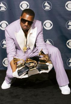 a man in a purple suit and white shoes sitting on a black carpet with his foot up