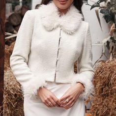 a woman standing in front of hay bales wearing a white coat with fur collar