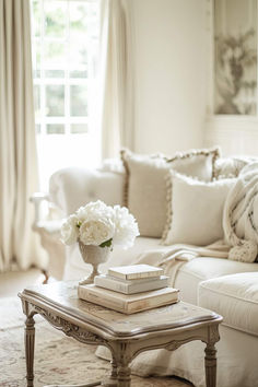 a living room filled with white furniture and flowers on top of a coffee table in front of a window