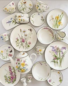 a table topped with lots of white plates and bowls filled with flowers on them next to a tea pot