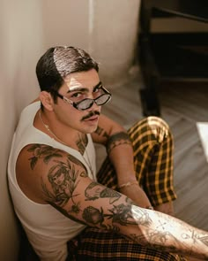 a man sitting on the floor with tattoos on his arms and legs, wearing glasses