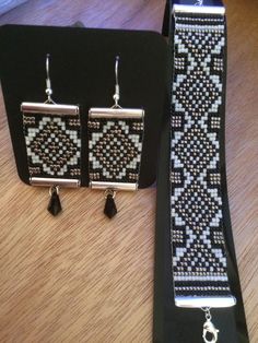 two pieces of jewelry sitting on top of a wooden table next to a pair of black and white earrings