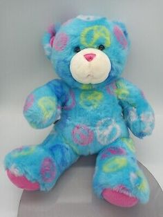 a blue and pink teddy bear sitting on top of a metal plate with a white background