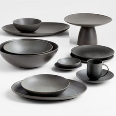 an assortment of black plates and cups on a white surface