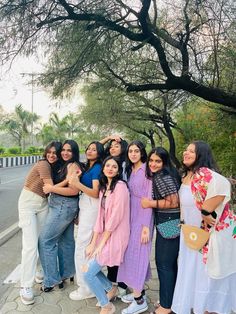 a group of women standing next to each other on the side of a road with trees in the background