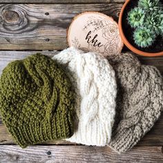 three knitted hats sitting on top of a wooden table next to a potted plant