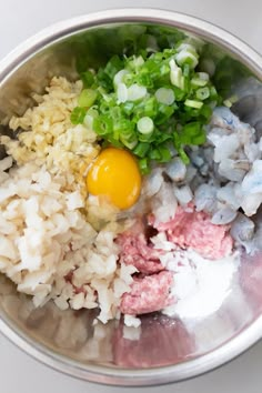 rice, meat and green onions in a metal bowl on a white table top with an egg