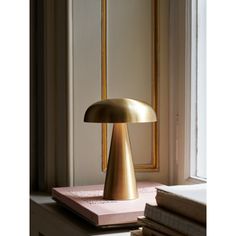 a gold lamp sitting on top of a table next to a window sill and books