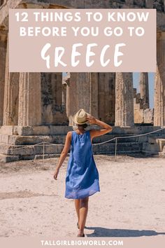 a woman in a blue dress and straw hat walking through the ruins of an ancient city