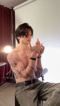 a shirtless man sitting in front of a mirror with tattoos on his arms and chest