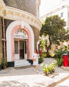 a woman standing in front of a pink and white building with the words grand hotel on it