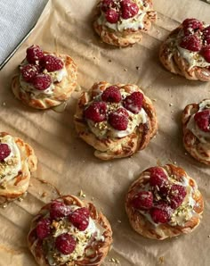 small pastries with raspberries and whipped cream on top are lined up on a piece of parchment paper