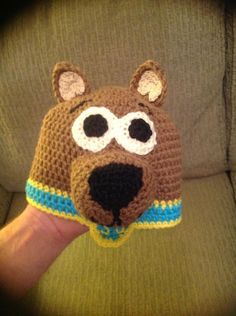 a crocheted bear hat with eyes and nose is held up to the camera