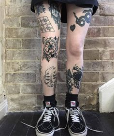 a person with tattoos on their legs standing in front of a brick wall