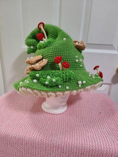 a knitted green hat with mushrooms on it sitting on top of a white table