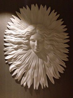 a white wall sculpture with a woman's face in the center and long flowing hair